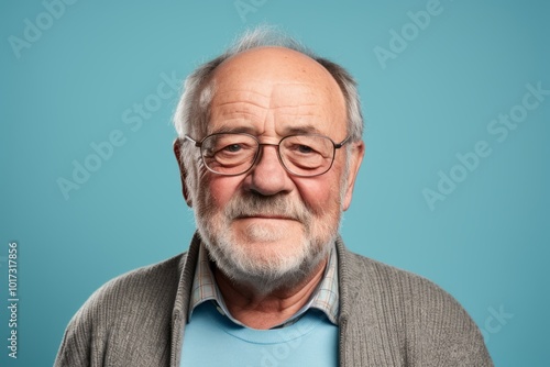 Portrait of a senior man with grey beard and glasses on blue background