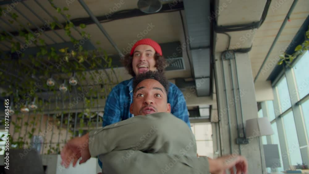 Happy male employee rides black colleague on chair in office Happy male employee rides black colleague on chair in office