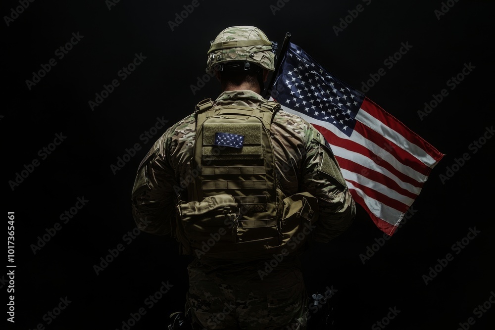 A soldier in camouflage uniform and helmet stands with his back to the camera holding a US flag. A soldier in camouflage uniform and helmet stands with his back to the camera holding a US flag.