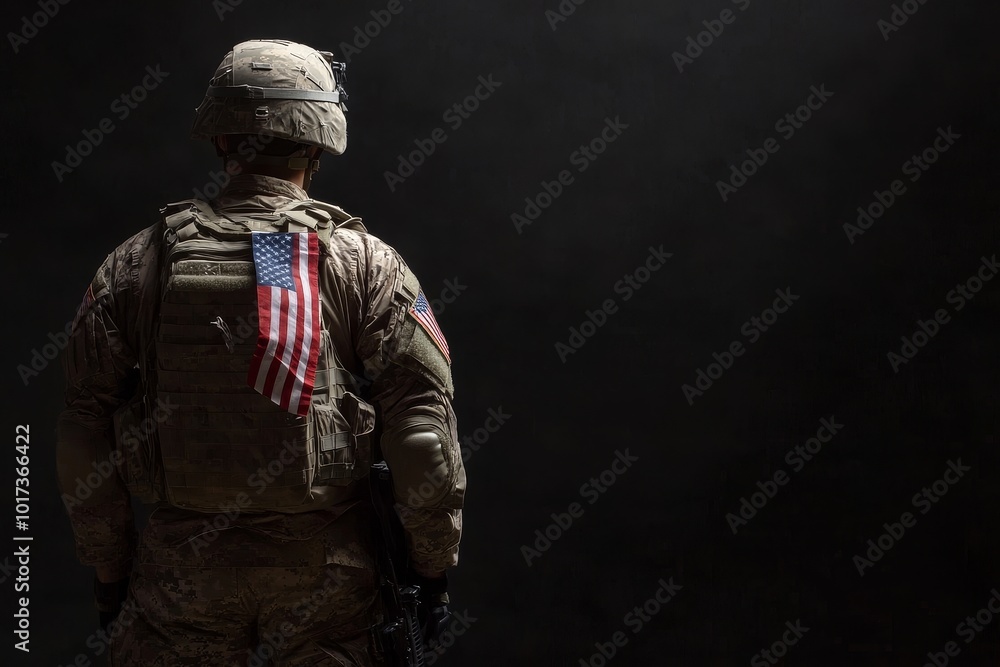 A soldier in full combat gear, stands with his back to the camera, with an American flag hanging from his tactical vest. A soldier in full combat gear, stands with his back to the camera, with an American flag hanging from his tactical vest.