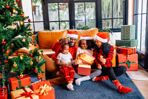 Multi-Generation Family Exchanging And Opening Gifts Around Christmas Tree At Home in Santa hat is holding box