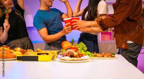 Four Asian friends, two men and two women, celebrate in an office party. They enjoy a fun-filled night with food, drinks, and laughter, bonding over teamwork and friendship. photo