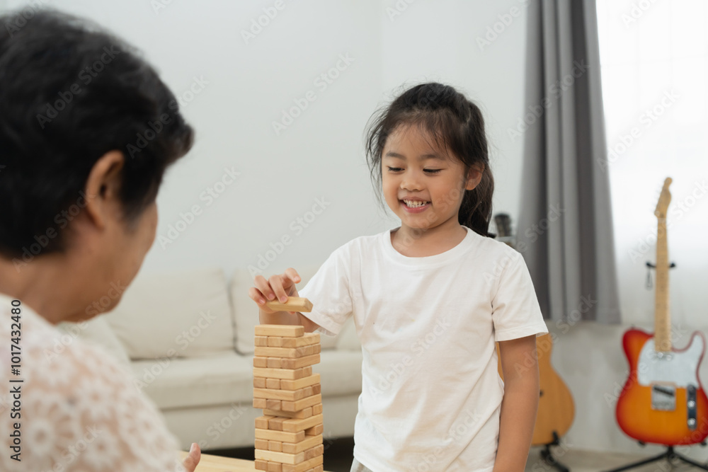 Asian woman and a young girl are playing with a wooden block tower. The girl is smiling and seems to be enjoying the game Asian woman and a young girl are playing with a wooden block tower. The girl is smiling and seems to be enjoying the game