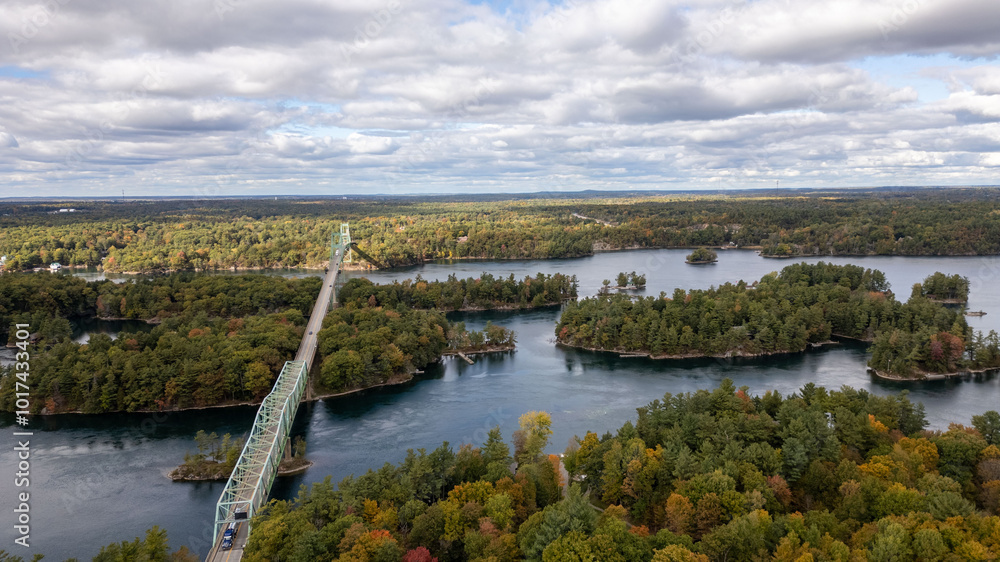 Fototapeta premium Aerial view of the Thousand Islands Bridge spanning over lush green islands and blue waters in the Thousand Islands region. This iconic bridge connects islands in Canada and the United States, showcas