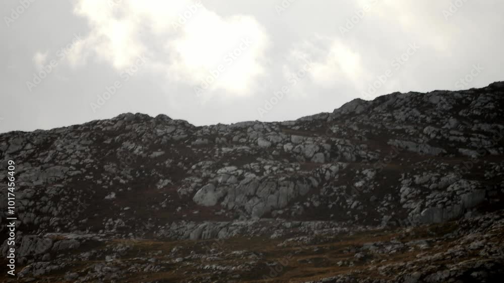 Atmospheric white clouds passing slowly above ominous rocky mountain peak