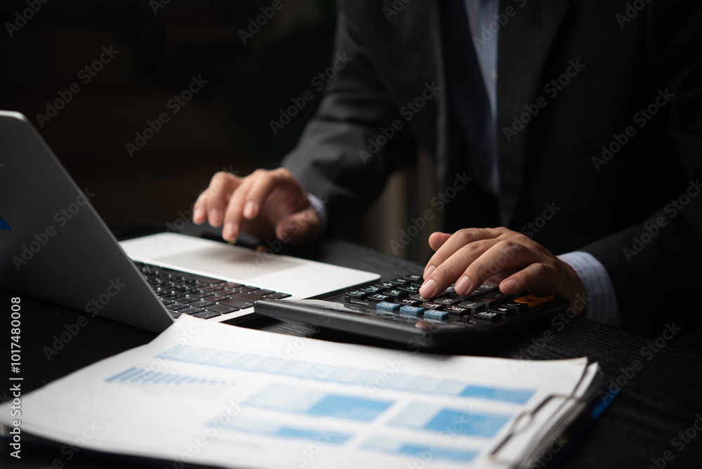 A businessman is using a calculator and laptop to analyze financial reports and data for business budgeting or planning bookkeeping payroll and budget tax. document finance accounting investment