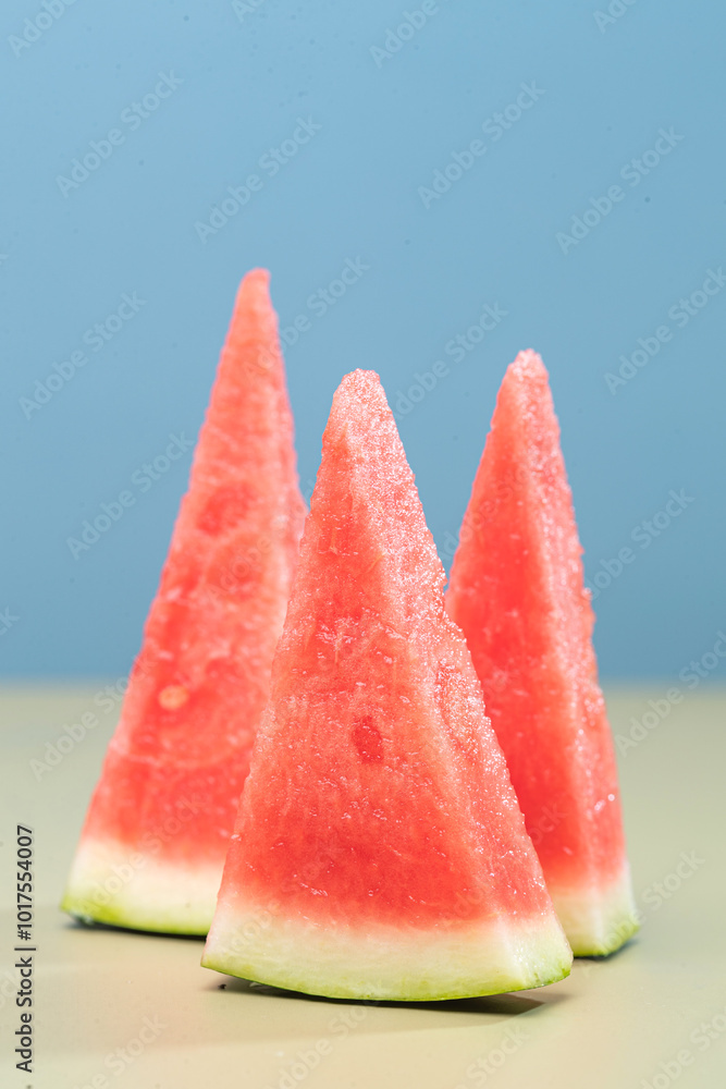 Three slices of watermelon arranged in a triangle shape on a light green background. The red fruit is juicy and refreshing, perfect for a summer snack. Three slices of watermelon arranged in a triangle shape on a light green background. The red fruit is juicy and refreshing, perfect for a summer snack.