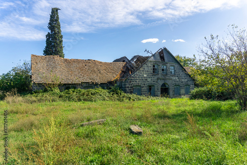 Exterior of abandoned German winery. Asureti, Georgia..Stone walls, arched entrance and windows. A yard overgrown with tall grass. Partially destroyed roof. Blue sky with clouds photo