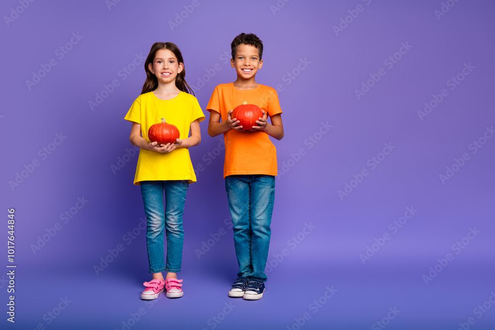 Full size photo of charming two little children hold halloween pumpkins wear trendy orange yellow outfit isolated on violet background Full size photo of charming two little children hold halloween pumpkins wear trendy orange yellow outfit isolated on violet background
