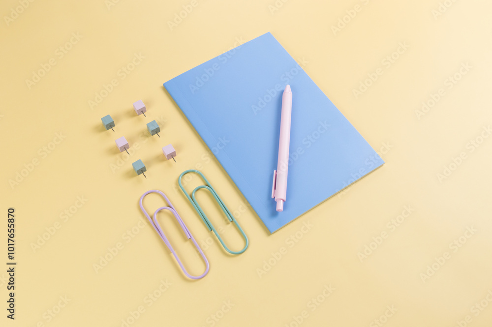 Top view of blue notebook on yellow background. Paperclips, pen and pins. School, office wallpaper. Flat lay, copy space. Top view of blue notebook on yellow background. Paperclips, pen and pins. School, office wallpaper. Flat lay, copy space.