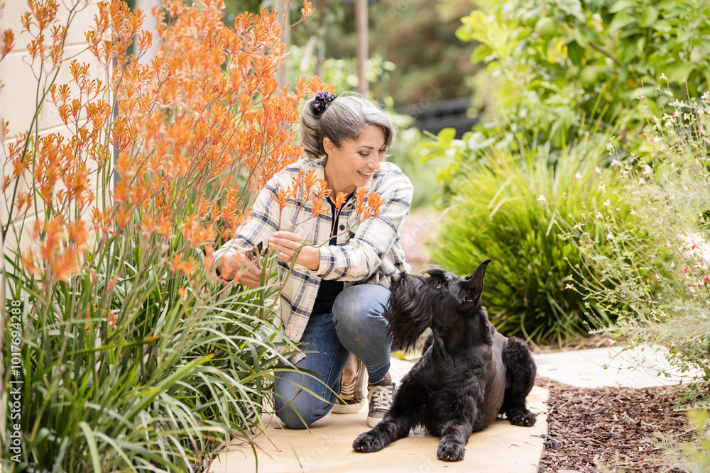 Woman and dog in garden together next to orange plant Woman and dog in garden together next to orange plant
