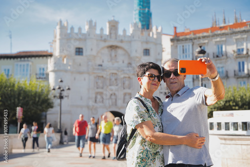 Happy mature couple taking a selfie with smartphone while visiting historic city center of Burgos during vacation