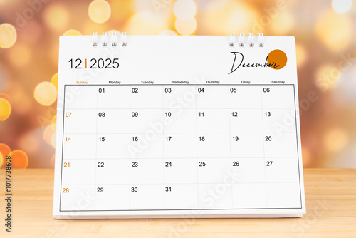 December 2025 desk calendar on wooden table with gold light bokeh background.