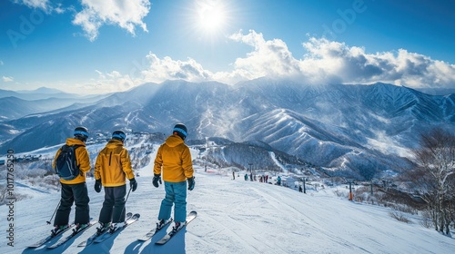 Snowboarders at the summit of Furano ski resort, gazing at the snow-covered Tokachidake range and Daisetsuzan mountains under a sun-filled sky.