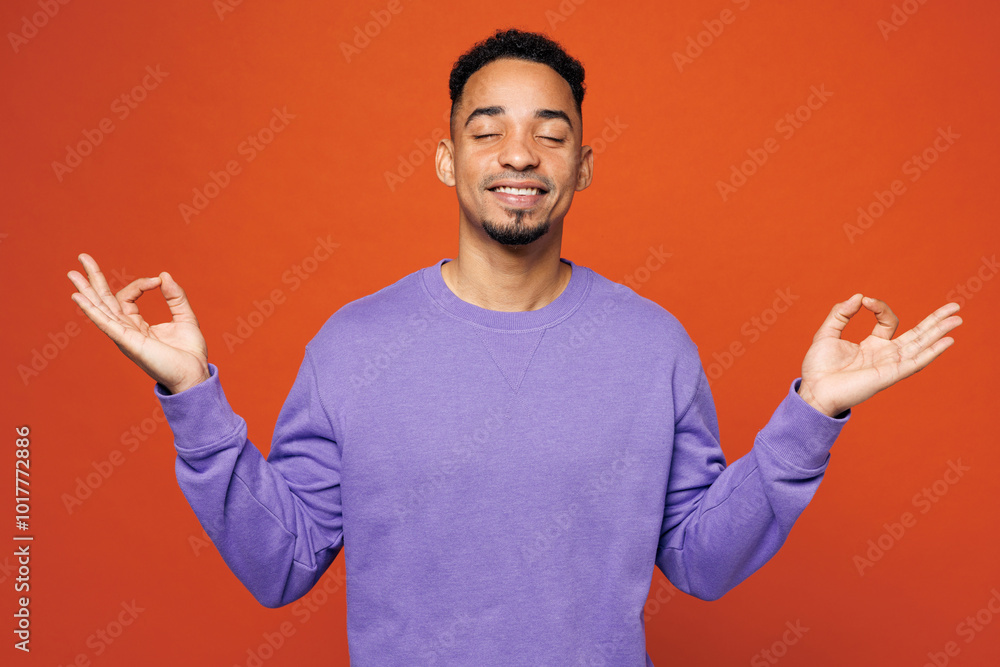Fototapeta premium Young man he wears purple sweatshirt casual clothes hold spreading hands in yoga om aum gesture relax meditate try to calm down close eyes isolated on plain red orange background. Lifestyle concept.