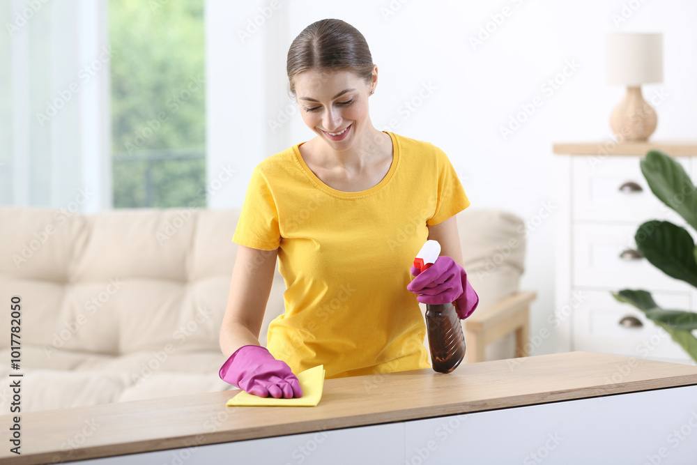Young woman cleaning wooden table with rag and spray at home Young woman cleaning wooden table with rag and spray at home