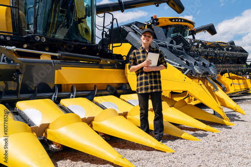 Obraz na plátně A woman with a digital tablet stands next to a yellow combine harvester at a farm equipment dealership