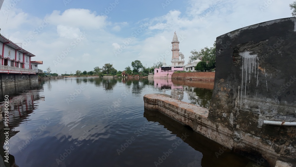 Tranquil pond in a village, showcasing a temple complex, embodying calmness and serving as a sacred pilgrimage destination. Haryana, India Tranquil pond in a village, showcasing a temple complex, embodying calmness and serving as a sacred pilgrimage destination. Haryana, India
