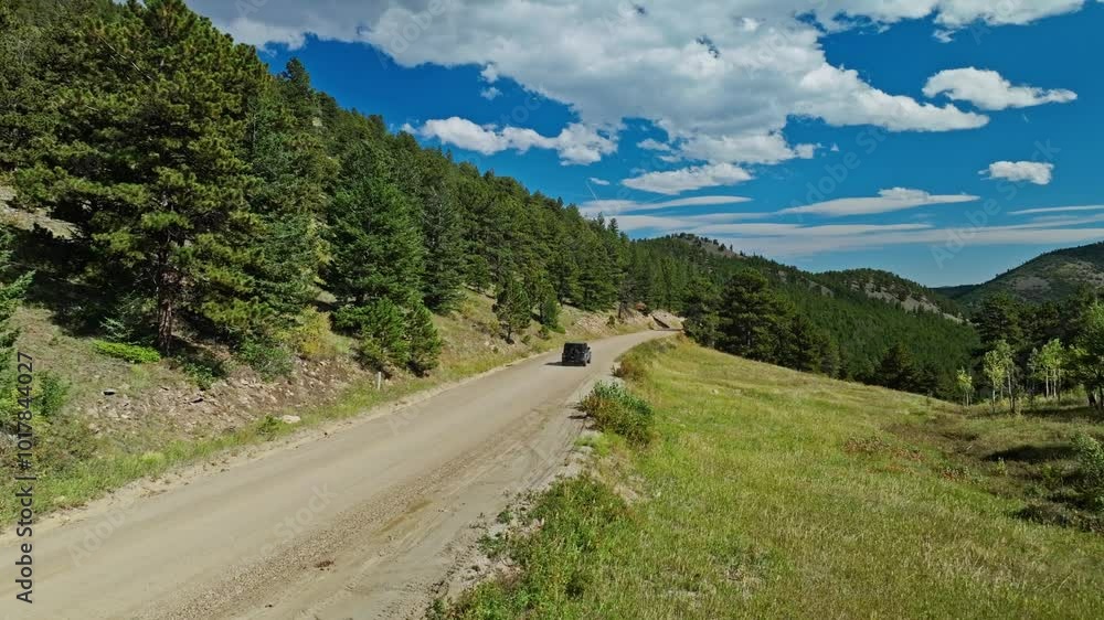 Drone angled rearview of a rugged vehicle driving along a dirt road cutting through a forested mountain area Drone angled rearview of a rugged vehicle driving along a dirt road cutting through a forested mountain area