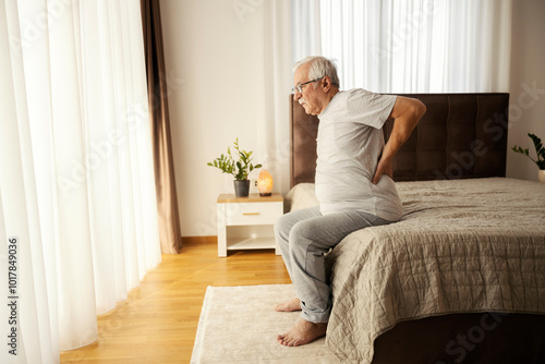 Tableau sur toile Senior man with backache trying to get up from the bed in the morning