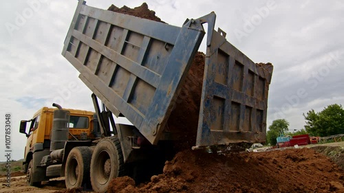 Dump truck unloading soil at a construction site. Close-up of dirt being tipped from the truck bed.