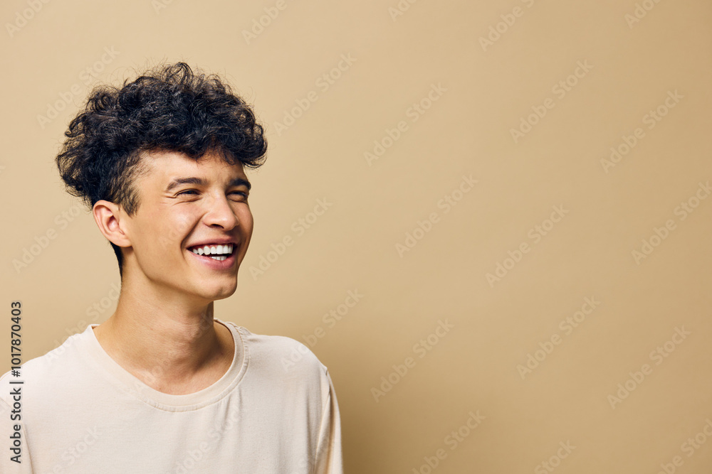 Young man smiling joyfully, showcasing positive emotions and happiness against a warm beige background Light, casual attire enhances the carefree vibe, perfect for lifestyle imagery Young man smiling joyfully, showcasing positive emotions and happiness against a warm beige background Light, casual attire enhances the carefree vibe, perfect for lifestyle imagery