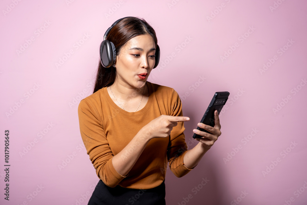 A woman is pointing at her cell phone while wearing headphones A woman is pointing at her cell phone while wearing headphones
