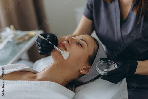 Cosmetologist performs a facial peeling procedure on a young woman.