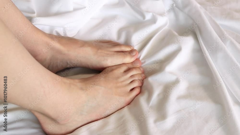 Female legs in bed on white sheets close-up. Female feet. Bare feet of a girl peeking out from under the blanket. Legs wiggling their toes on white bed linen. Rest Female legs in bed on white sheets close-up. Female feet. Bare feet of a girl peeking out from under the blanket. Legs wiggling their toes on white bed linen. Rest