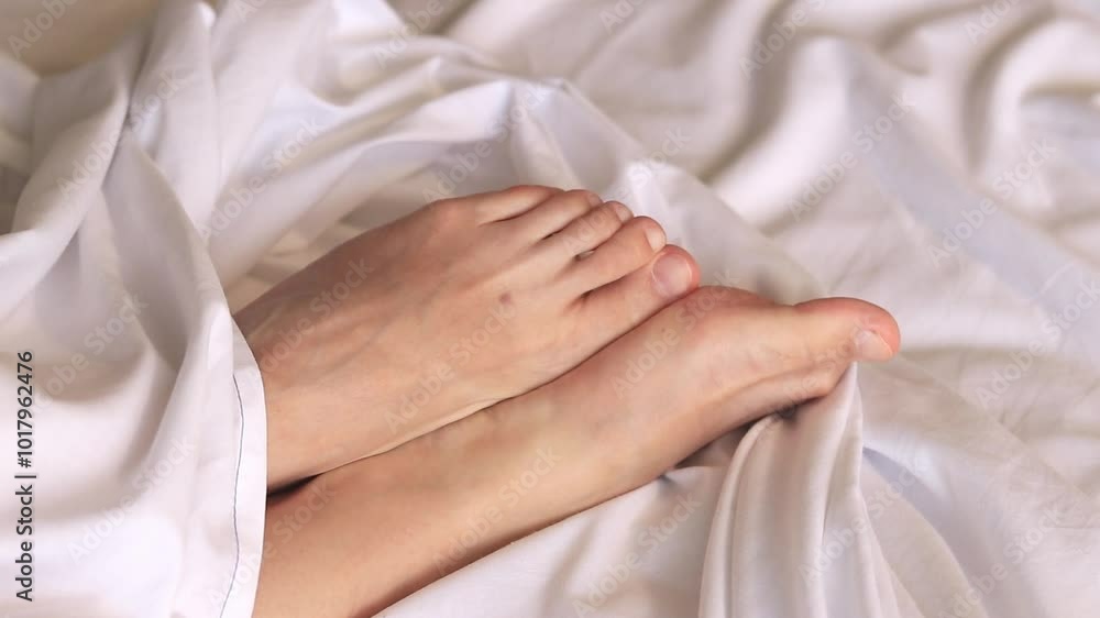 Female legs in bed on white sheets close-up. Female feet. Bare feet of a girl peeking out from under the blanket. Legs wiggling their toes on white bed linen. Rest Female legs in bed on white sheets close-up. Female feet. Bare feet of a girl peeking out from under the blanket. Legs wiggling their toes on white bed linen. Rest