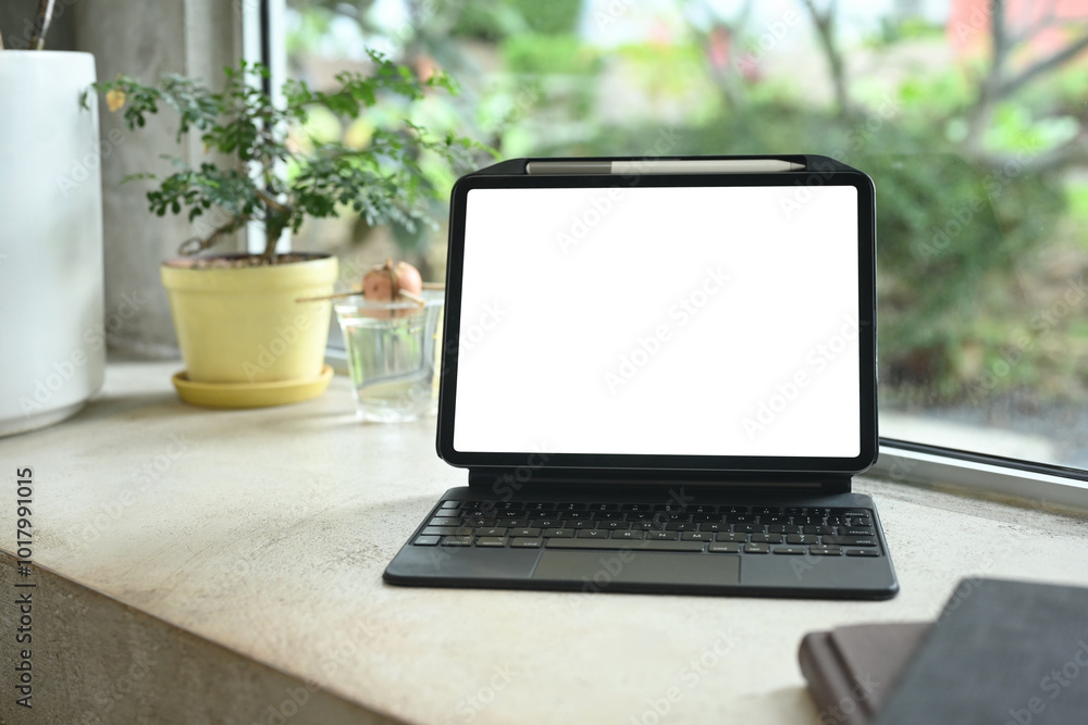Digital tablet with blank screen on a table next to a potted plant and notebooks Digital tablet with blank screen on a table next to a potted plant and notebooks
