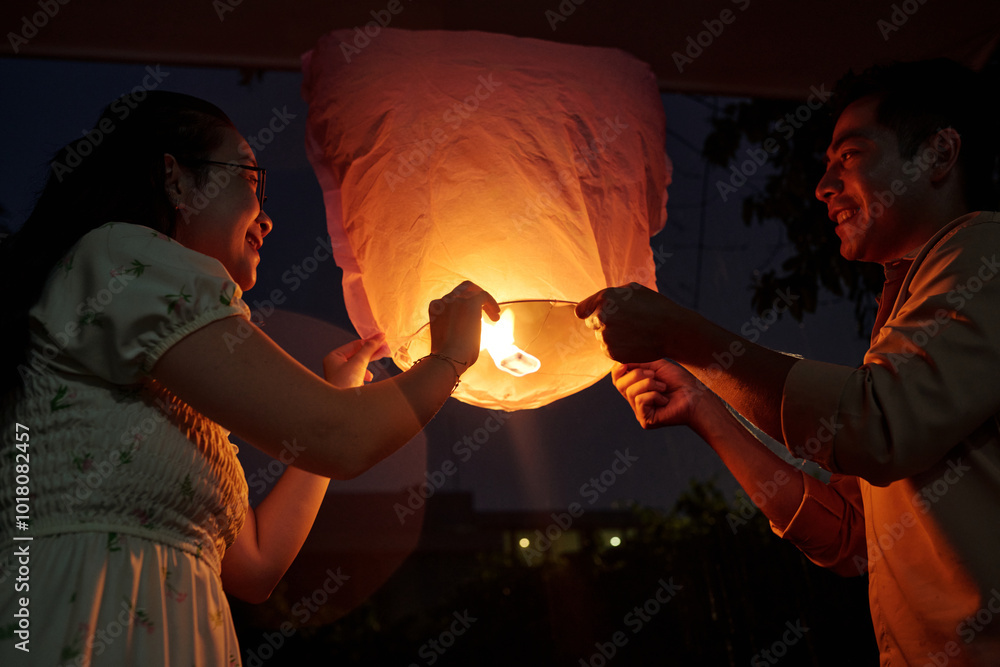 Obraz premium Happy Asian couple launching lantern outdoors and celebrating holiday