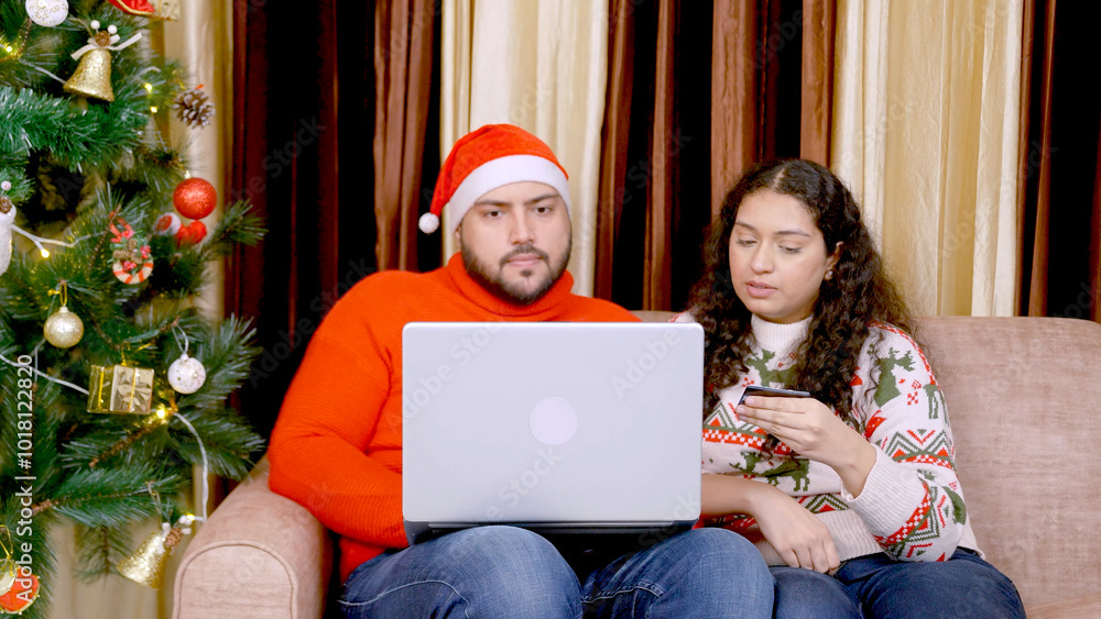 Indian Couple Sitting on Couch Adding Credit Card Details for Christmas Shopping Indian Couple Sitting on Couch Adding Credit Card Details for Christmas Shopping