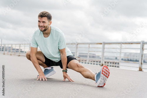 A Man Performing a Dynamic Stretching Exercise Outdoors on a Cloudy Day Near a Waterfront photo