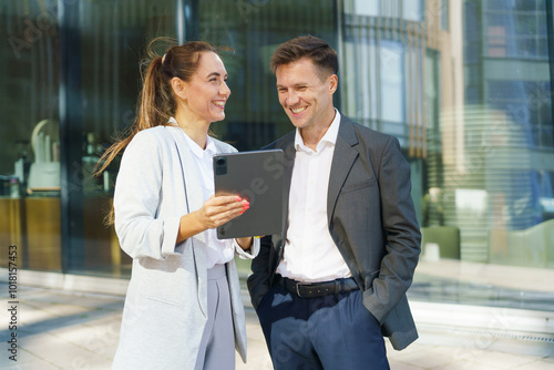 Professionals Collaborating With a Tablet Outside a Modern Office Building in Bright Daylight, Sharing Ideas and Smiles