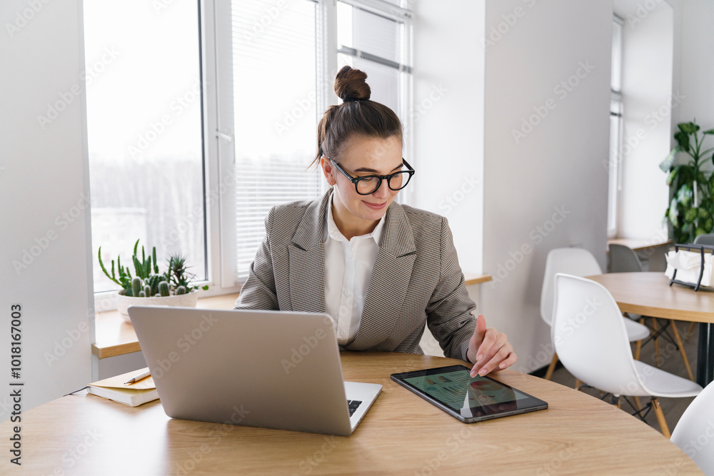 A Professional Woman Works on a Tablet While Sitting at a Modern Office Table During the Day A Professional Woman Works on a Tablet While Sitting at a Modern Office Table During the Day