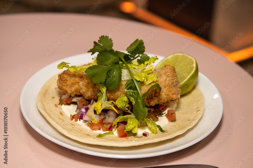 A delicious plate of Cornish Cod Tacos with a slice of Lime on a pink wooden kitchen table or work top A delicious plate of Cornish Cod Tacos with a slice of Lime on a pink wooden kitchen table or work top