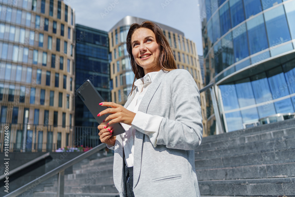 Professional Woman Holding a Tablet While Standing on Steps of a Modern Building in an Urban Environment During Daytime Professional Woman Holding a Tablet While Standing on Steps of a Modern Building in an Urban Environment During Daytime