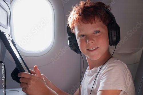 Young boy enjoys entertainment on a plane, looking at camera photo