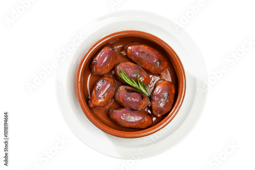 Overhead shot of a small casserole dish on a white plate with blood sausages and rosemary on a white background