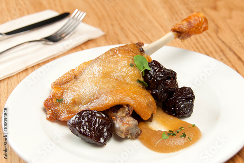 White plate of chicken in its sauce with plums with forks and napkin on wooden background