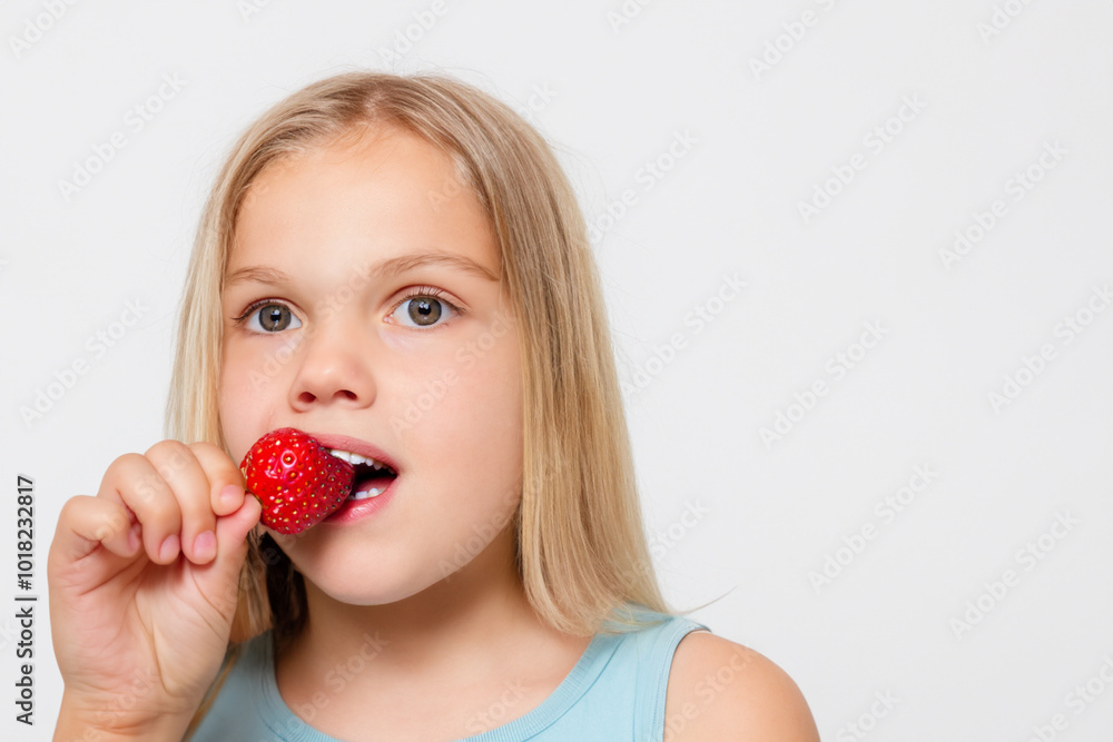 Girl is eating strawberries on white . food young fruit concept. girl in gray eating strawberries on a . a girl eating strawberries on a white with a gray lifestyle. Girl is eating strawberries on white . food young fruit concept. girl in gray eating strawberries on a . a girl eating strawberries on a white with a gray lifestyle.
