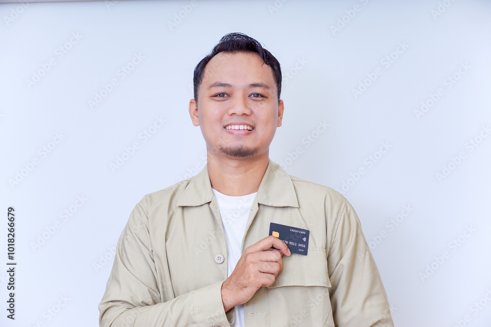 A young man in a beige jacket proudly displays his credit card A young man in a beige jacket proudly displays his credit card