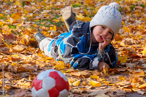 Obraz na płótnie Child boy in autumn park with foliage. He lies on the yellow leaves. High quality photo w salonie