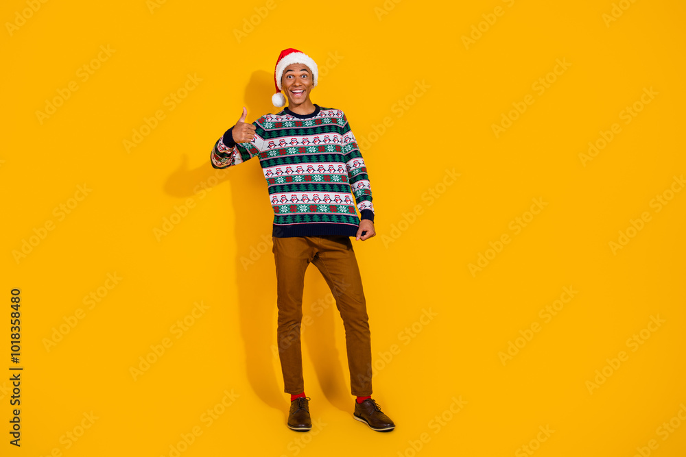 Full length photo of young guy show ugly sweater thumb up dressed ornament christmas garment celebrate winter holidays on yellow background Full length photo of young guy show ugly sweater thumb up dressed ornament christmas garment celebrate winter holidays on yellow background