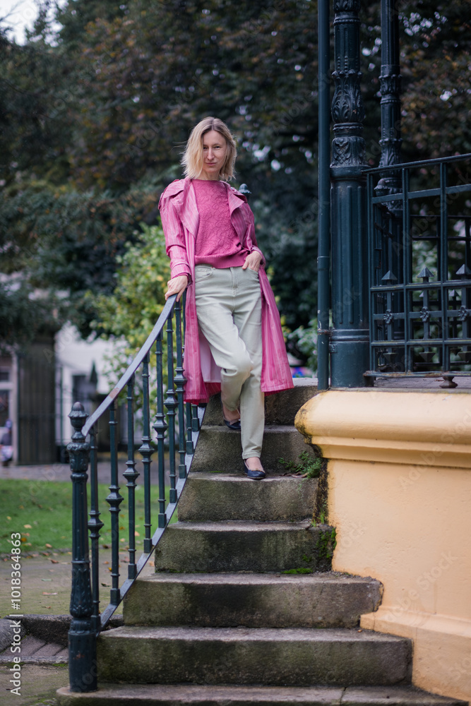 A woman in a pink coat stands on stone steps in a park during autumn, with the overcast weather adding a calm and reflective atmosphere. A woman in a pink coat stands on stone steps in a park during autumn, with the overcast weather adding a calm and reflective atmosphere.