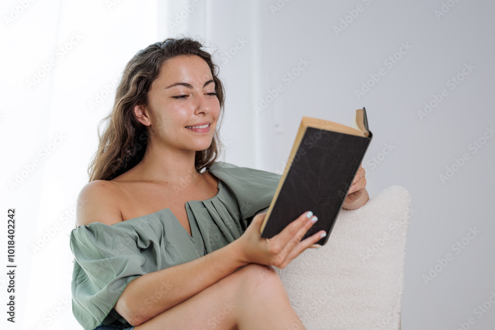 Young girl reading an interesting book. Young woman entertains herself by reading a book. She smiles because she likes the story of the book and imagines the protagonists. Young girl reading an interesting book. Young woman entertains herself by reading a book. She smiles because she likes the story of the book and imagines the protagonists.