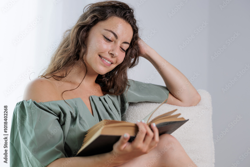Young girl reading an interesting book. Young woman entertains herself by reading a book. She smiles because she likes the story of the book and imagines the protagonists. Young girl reading an interesting book. Young woman entertains herself by reading a book. She smiles because she likes the story of the book and imagines the protagonists.