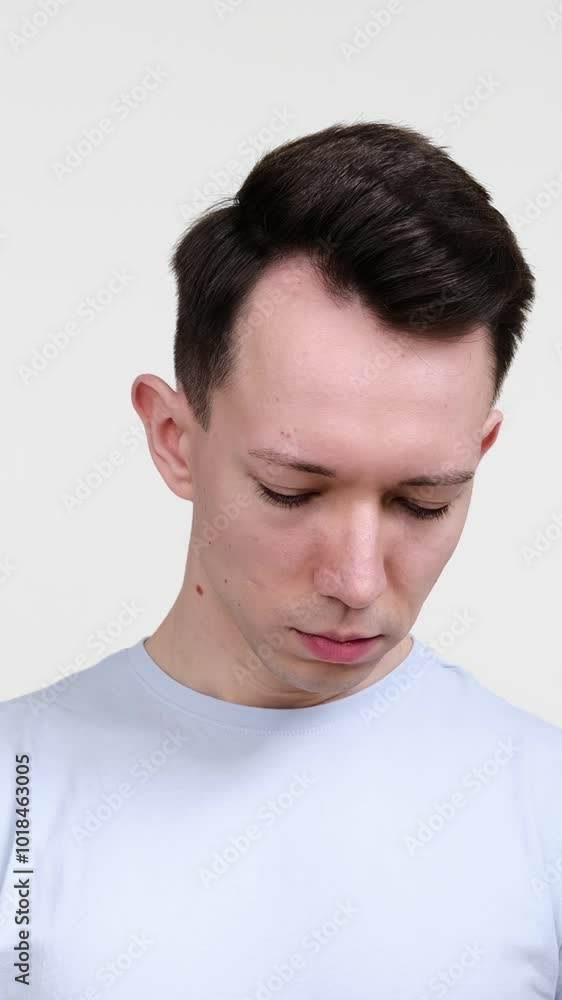 Portrait of a young adult Caucasian upset and sad man, standing on white background. Concept of a tension and emotional stress. Vertical video. Portrait of a young adult Caucasian upset and sad man, standing on white background. Concept of a tension and emotional stress. Vertical video.