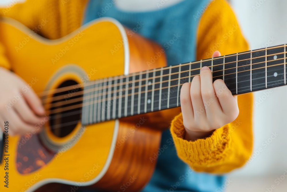 Fototapeta premium Close-up of a child playing an acoustic guitar, wearing a yellow jacket.